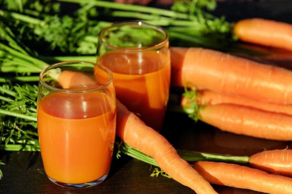 Vaso de jugo de zanahoria, naranja y mango sobre tabla de madera con zanahorias y naranjas frescas alrededor