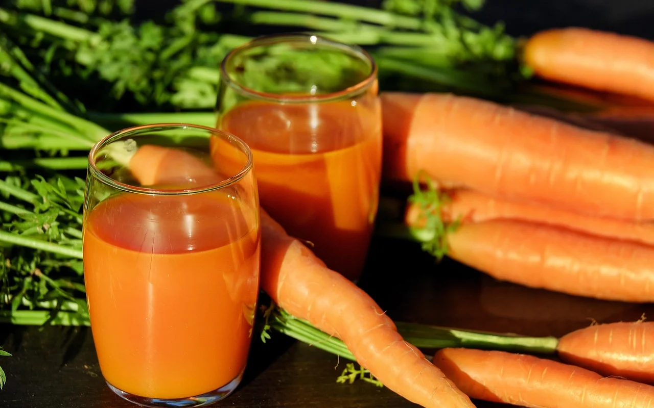 Vaso de jugo de zanahoria, naranja y mango sobre tabla de madera con zanahorias y naranjas frescas alrededor